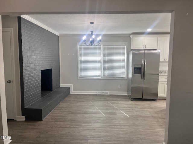 kitchen featuring a fireplace, crown molding, visible vents, white cabinetry, and stainless steel fridge with ice dispenser