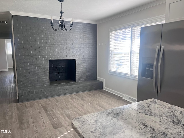 interior space with crown molding, wood finished floors, baseboards, a brick fireplace, and an inviting chandelier