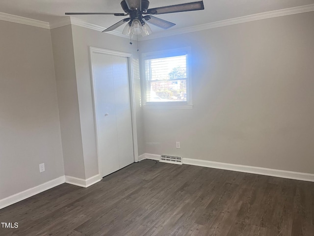 empty room featuring baseboards, visible vents, dark wood finished floors, and crown molding