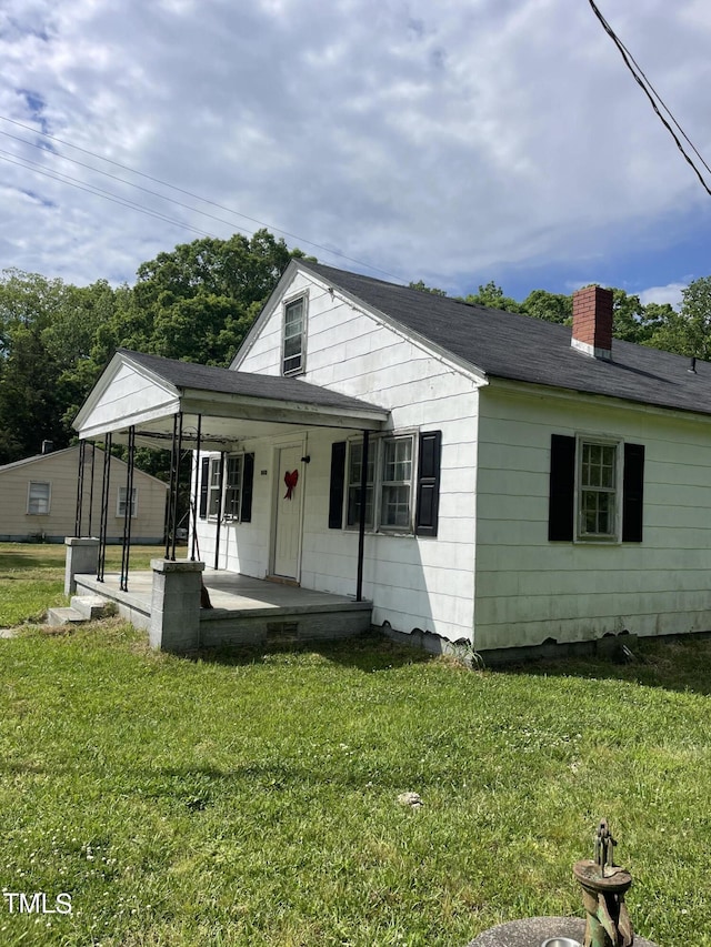 view of front of house featuring a porch, a front yard, roof with shingles, and a chimney