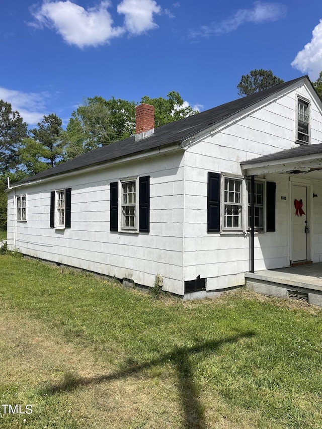 view of side of home featuring a porch, a lawn, and a chimney