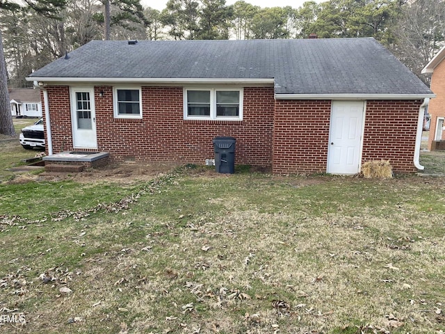 back of property with brick siding, a yard, and roof with shingles