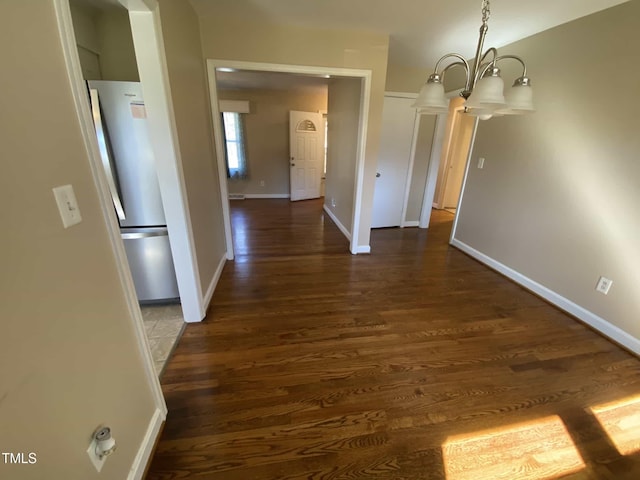 unfurnished dining area with a chandelier, dark wood finished floors, and baseboards