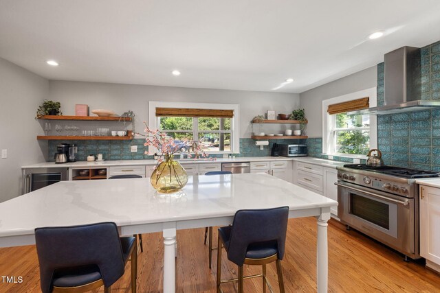 kitchen with a healthy amount of sunlight, open shelves, stainless steel appliances, and wall chimney exhaust hood