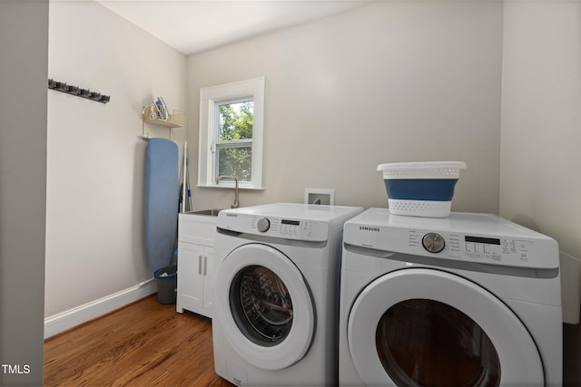 washroom featuring washing machine and dryer, cabinet space, a sink, baseboards, and light wood finished floors