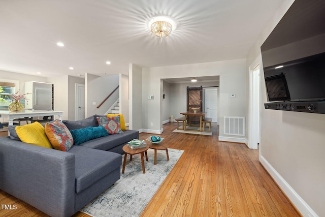 living room with visible vents, light wood-type flooring, a barn door, stairway, and baseboards