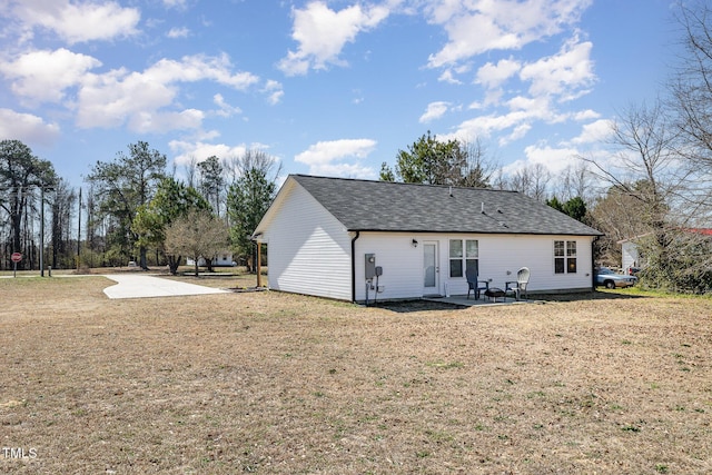 rear view of house with a yard, roof with shingles, and a patio