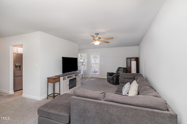 living room featuring light carpet, ceiling fan, a fireplace, and baseboards