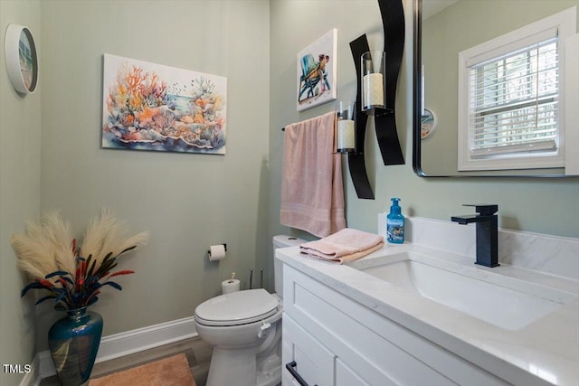 half bathroom featuring toilet, baseboards, wood finished floors, and vanity