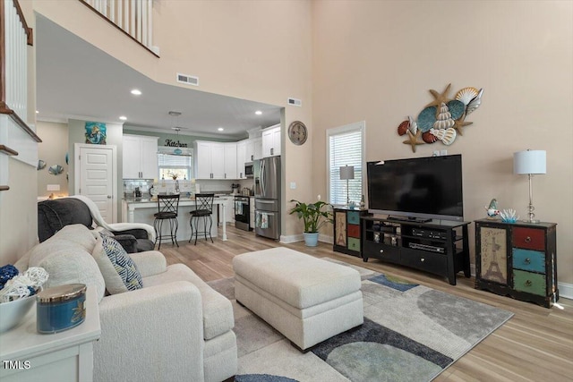 living room with light wood-style floors, visible vents, and a wealth of natural light