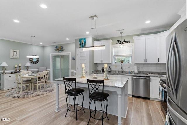 kitchen featuring light stone counters, a breakfast bar, a sink, white cabinetry, and appliances with stainless steel finishes