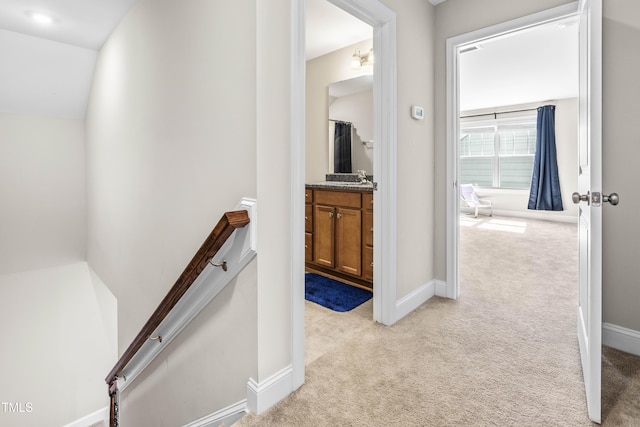 corridor with baseboards, a sink, an upstairs landing, and light colored carpet