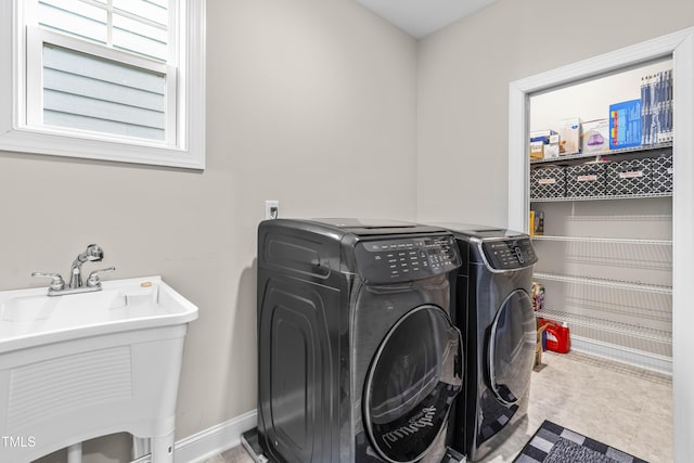 clothes washing area featuring laundry area, baseboards, tile patterned floors, washing machine and clothes dryer, and a sink