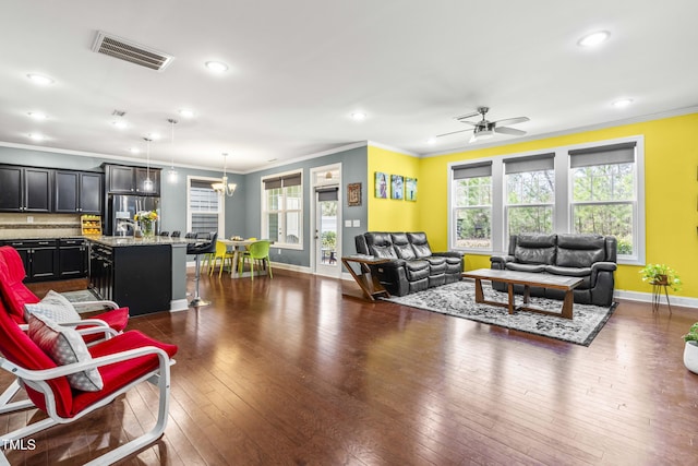 living room featuring dark wood-style floors, visible vents, ornamental molding, baseboards, and ceiling fan with notable chandelier