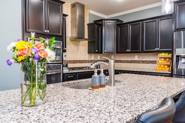 kitchen featuring stainless steel appliances, a sink, ornamental molding, wall chimney range hood, and tasteful backsplash