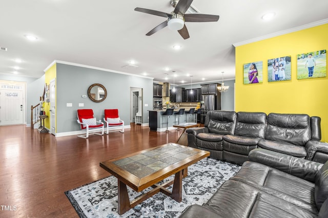 living area featuring ceiling fan with notable chandelier, baseboards, stairway, dark wood-style floors, and crown molding