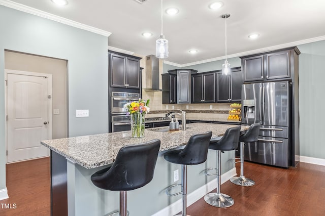 kitchen featuring dark wood-style flooring, a sink, appliances with stainless steel finishes, wall chimney range hood, and light stone countertops