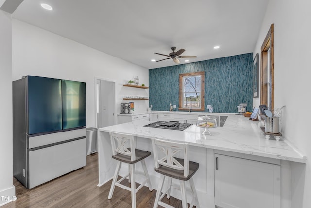 kitchen with appliances with stainless steel finishes, light stone counters, wood finished floors, open shelves, and recessed lighting