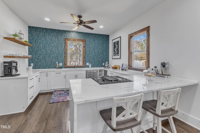 kitchen with light stone counters, a peninsula, gas cooktop, open shelves, and a sink