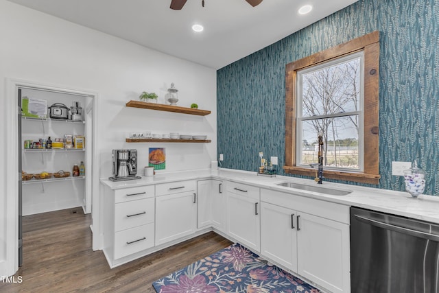 kitchen with dark wood-style flooring, stainless steel dishwasher, a sink, light stone countertops, and wallpapered walls