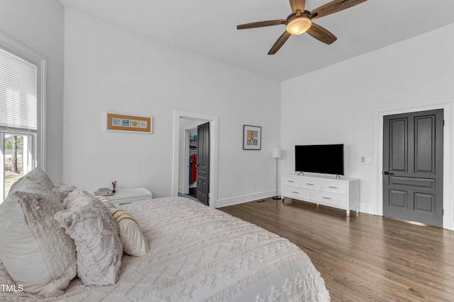 bedroom featuring a walk in closet, ceiling fan, baseboards, and wood finished floors