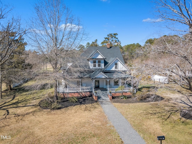 view of front facade with driveway, a chimney, roof with shingles, covered porch, and a front lawn