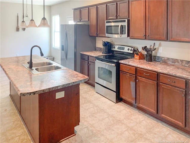 kitchen featuring an island with sink, appliances with stainless steel finishes, decorative light fixtures, light countertops, and a sink