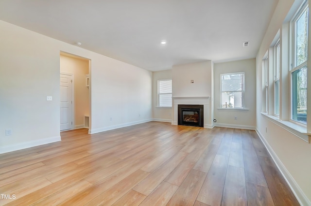 unfurnished living room with a wealth of natural light, a glass covered fireplace, light wood-style flooring, and baseboards