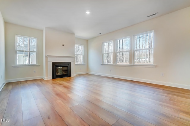 unfurnished living room with a wealth of natural light, a glass covered fireplace, visible vents, and light wood finished floors