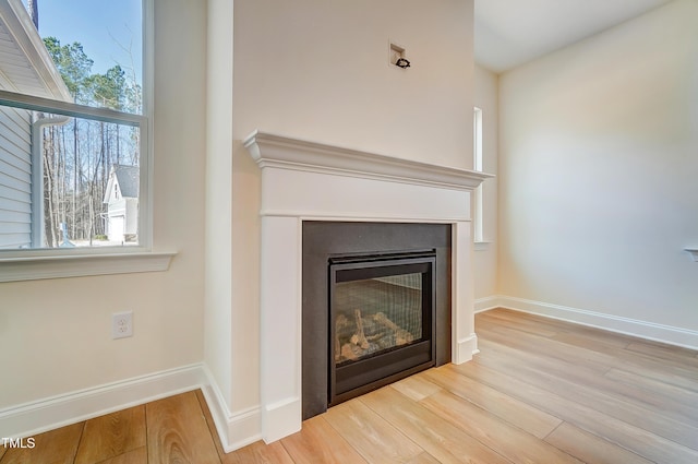 details with wood finished floors, a glass covered fireplace, and baseboards