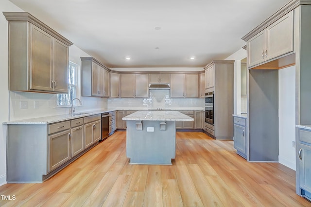 kitchen with tasteful backsplash, a center island, light wood-type flooring, under cabinet range hood, and a sink