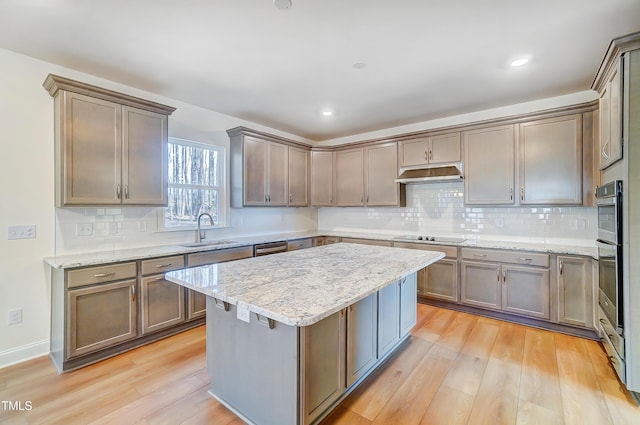 kitchen with a center island, light wood-style floors, a sink, under cabinet range hood, and black electric cooktop