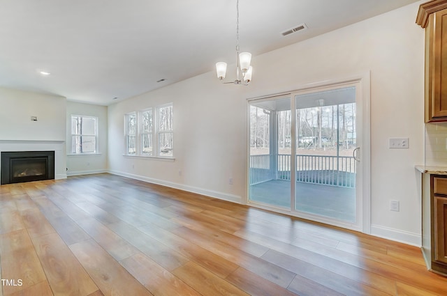 unfurnished living room featuring light wood-type flooring, a glass covered fireplace, visible vents, and baseboards