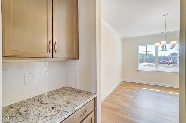 kitchen with light stone counters, a notable chandelier, ornamental molding, light wood-type flooring, and tasteful backsplash