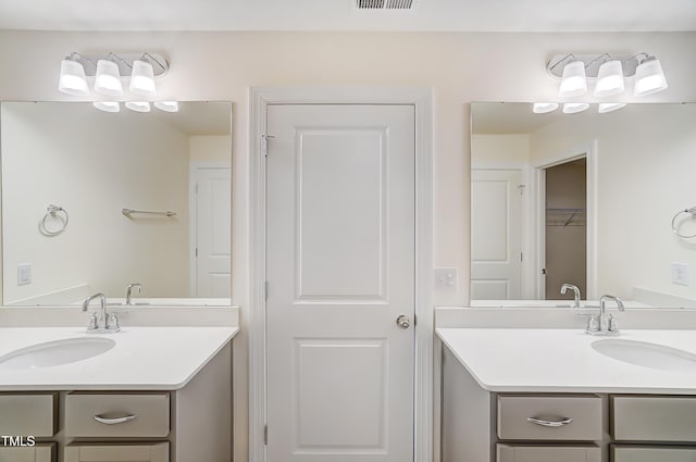 bathroom featuring a closet, two vanities, and a sink