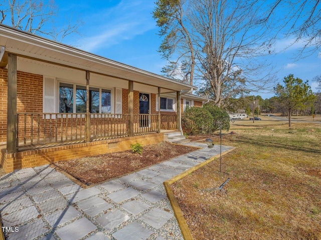 view of front of home featuring covered porch, brick siding, and a front lawn