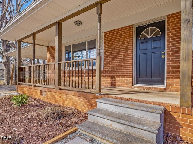 doorway to property with a porch and brick siding