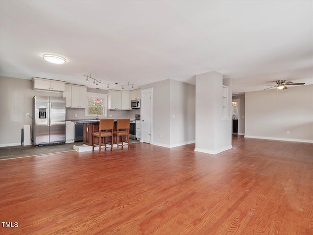 unfurnished living room featuring light wood finished floors, baseboards, a ceiling fan, and rail lighting