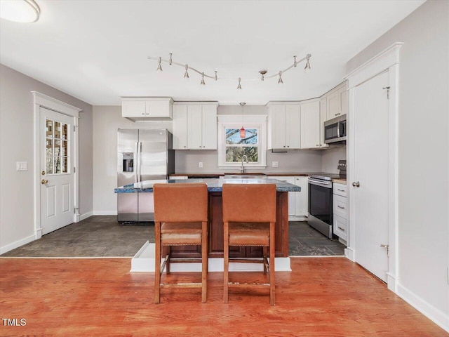 kitchen with a breakfast bar, a sink, white cabinetry, appliances with stainless steel finishes, and a center island