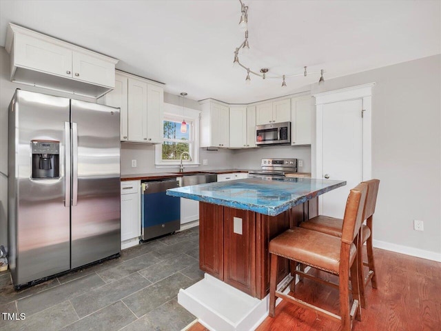 kitchen featuring a kitchen bar, appliances with stainless steel finishes, white cabinets, a kitchen island, and baseboards