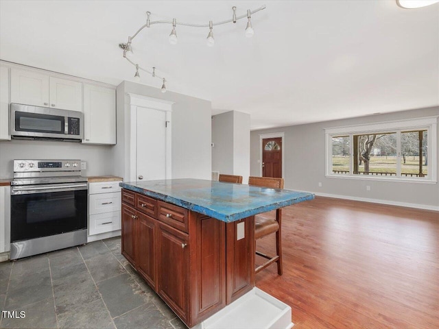 kitchen with baseboards, appliances with stainless steel finishes, a kitchen breakfast bar, open floor plan, and white cabinetry