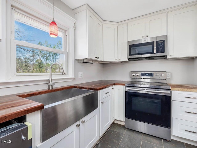 kitchen featuring butcher block counters, appliances with stainless steel finishes, decorative light fixtures, white cabinetry, and a sink