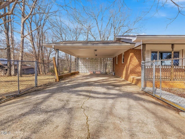 view of car parking with driveway, fence, and a carport