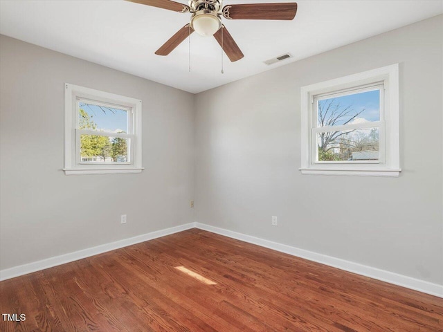 spare room with a ceiling fan, wood finished floors, visible vents, and baseboards