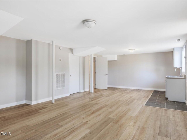 unfurnished living room with light wood-style floors, baseboards, visible vents, and a sink