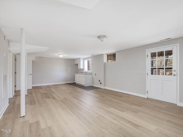 unfurnished living room featuring light wood-type flooring, a sink, visible vents, and baseboards