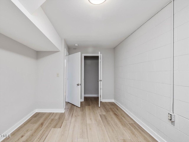 spare room featuring concrete block wall, light wood-style flooring, and baseboards