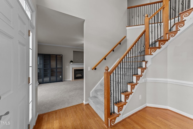 staircase with carpet, crown molding, a fireplace, wood finished floors, and baseboards