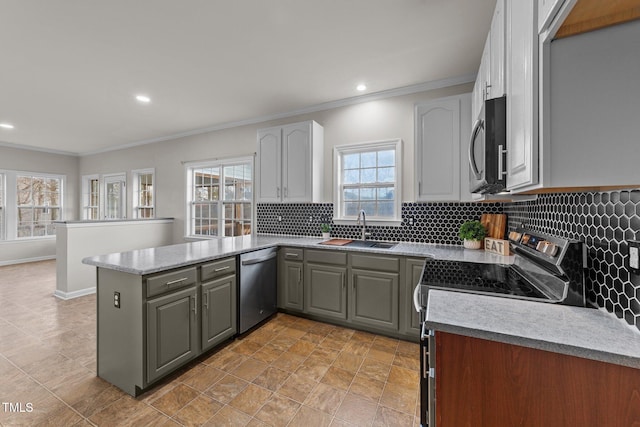 kitchen with a peninsula, a sink, ornamental molding, appliances with stainless steel finishes, and tasteful backsplash