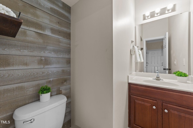 half bath featuring vanity, toilet, and wooden walls